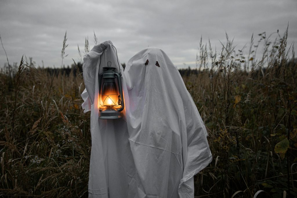 A ghostly figure holds a lantern in a dark, spooky field, embodying Halloween spirit.